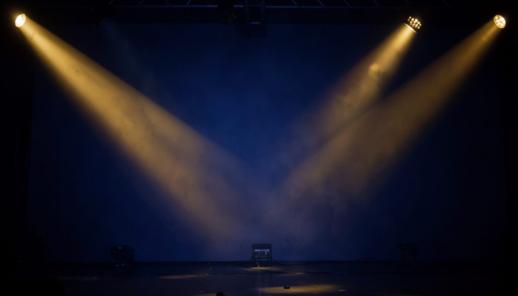 Empty stage with crossing spotlight beams against a blue backdrop, dark and dramatic mood